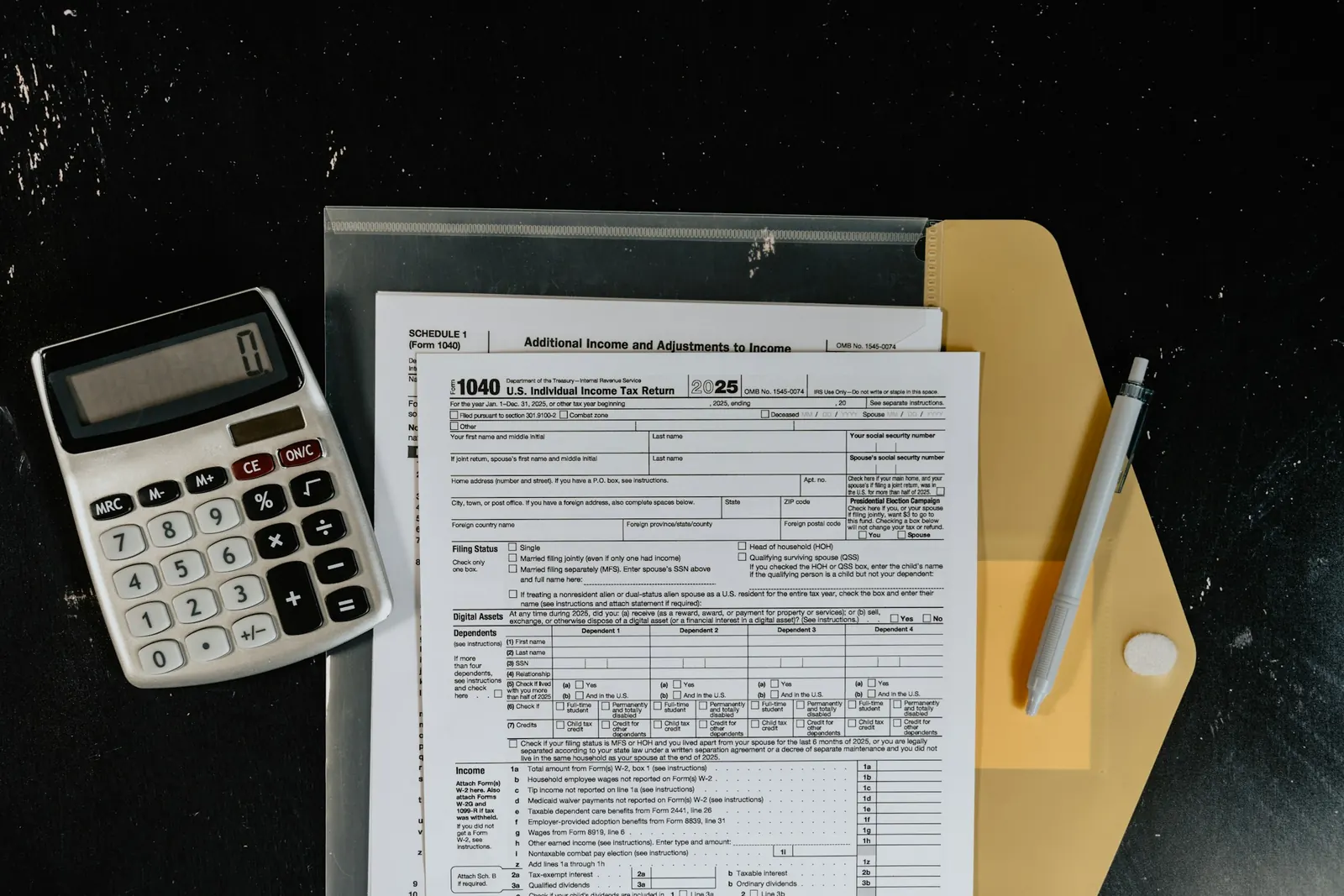 Tax forms, a calculator, and a pen on a dark desk
